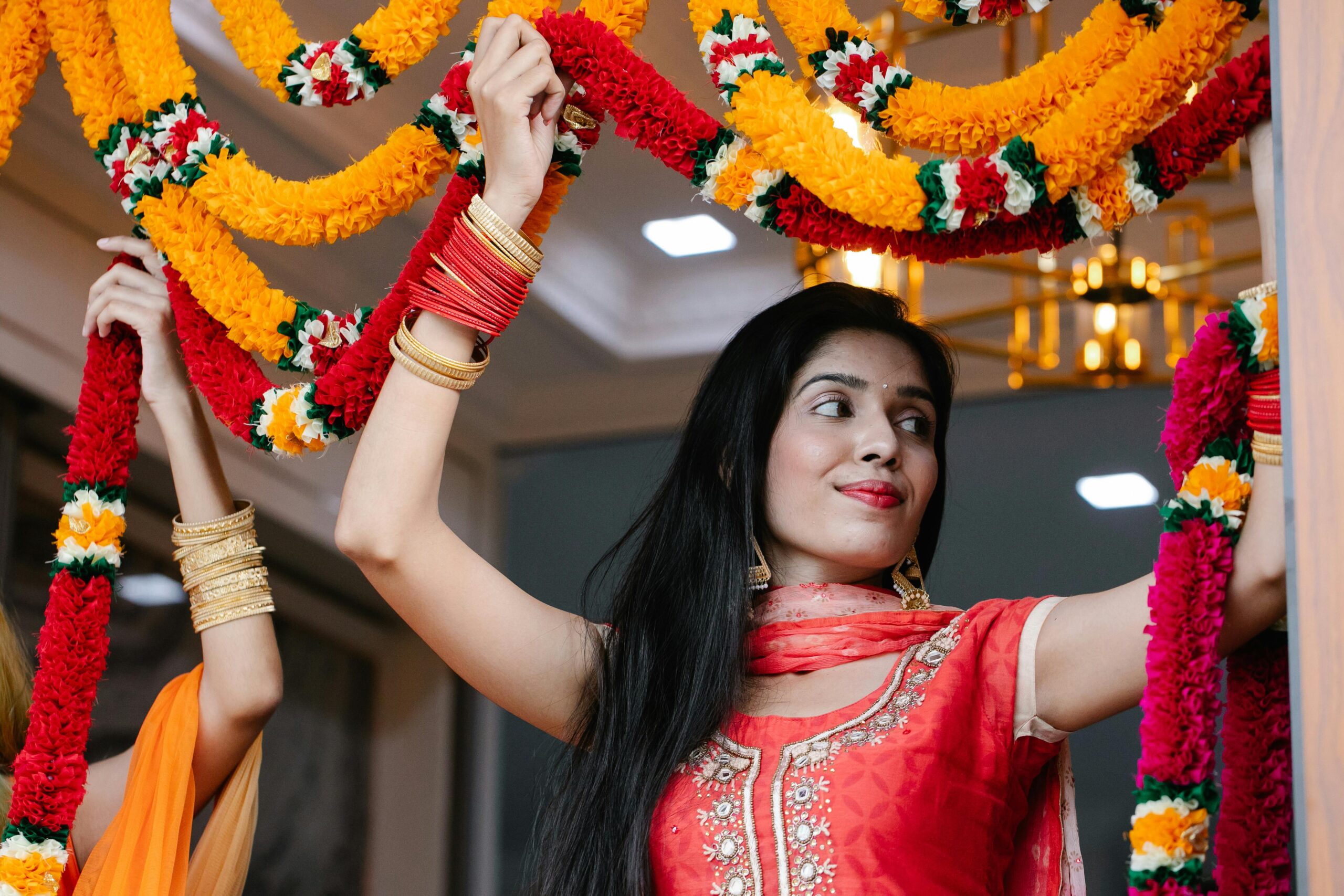 Woman in traditional attire posing with colorful garlands indoors, showcasing festival decor.